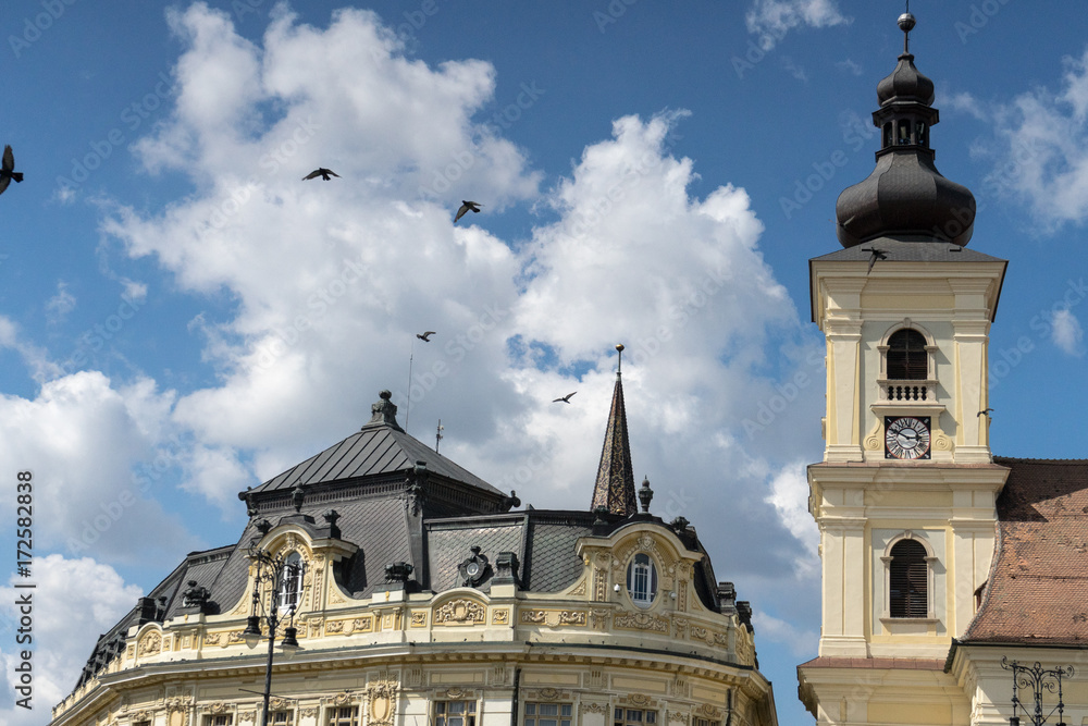 Flying pigeons on a cloudy blues sky over the top of buildings in center of Sibiu, Romania