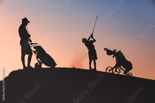 silhouettes of man with his son golfers playing golf on golf course at sunset
