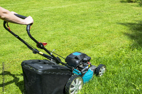 Beautiful girl cuts the lawn. Mowing lawns. Lawn mower on green grass. mower grass equipment. mowing gardener care work tool close up view sunny day