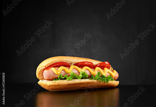 Photographie Big hotdog with sausage tomatoes, mustard and salad isolated on black background