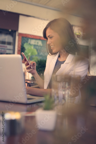 Business woman holding cup of coffee and using laptop and smart phone.