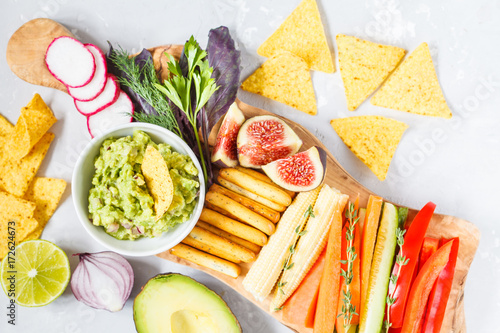 guacamole with vegetables and snacks on a wooden board