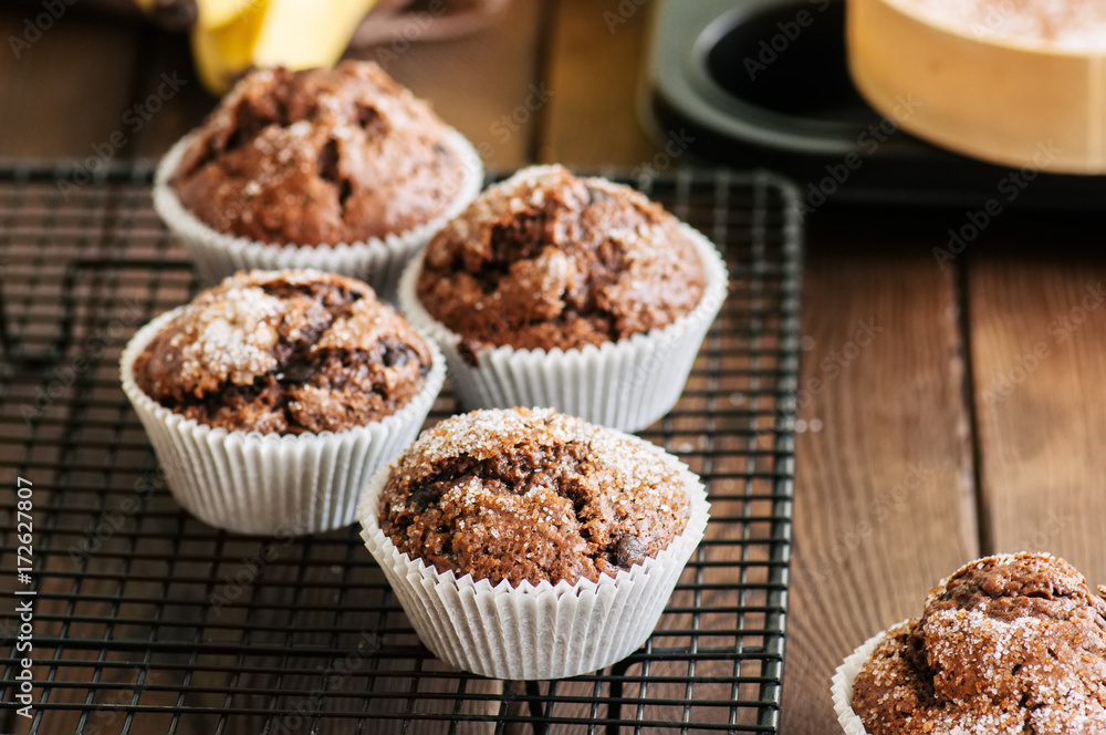 Homemade banana chocolate muffins sprinkled with sugar on a wooden background. Homemade banana chocolate muffins sprinkled with sugar on a wooden background.