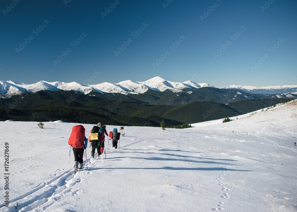 Group of tourists walks on a mountain hill in winter. Mountain range covered with snow at the background