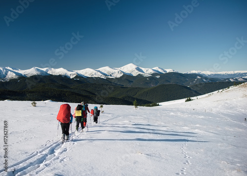 Group of tourists walks on a mountain hill in winter. Mountain range covered with snow at the background © ianachyrva