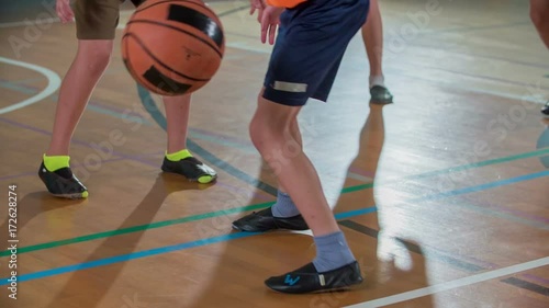 The orange team is having a ball. The boys are playing basketball in a school gym.