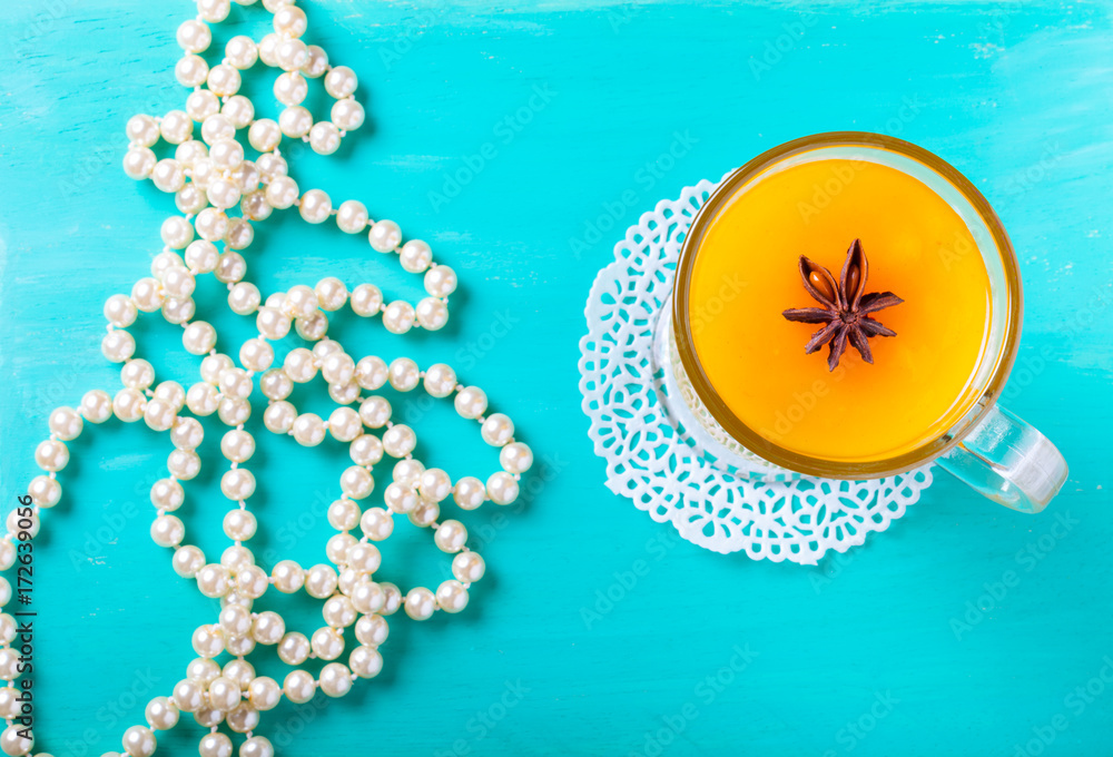 Naklejka premium Glass of sea buckthorn beverage (kissel) and pearl beads on a bright blue wooden table or board for background. New year theme