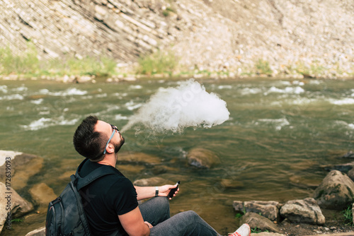 Young traveler smoke electronic cigarette near mountain river