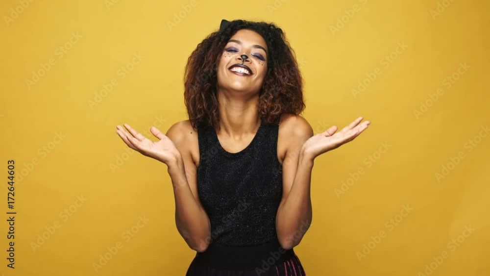 Tricky funny woman in haloween cat costume holding her heand together and smiling angrily to camera isolated over yellow Tricky funny woman in haloween cat costume holding her heand together and smiling angrily to camera isolated over yellow