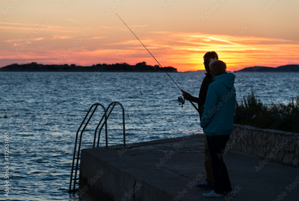 Silhouette of adult couple fishing at sunset