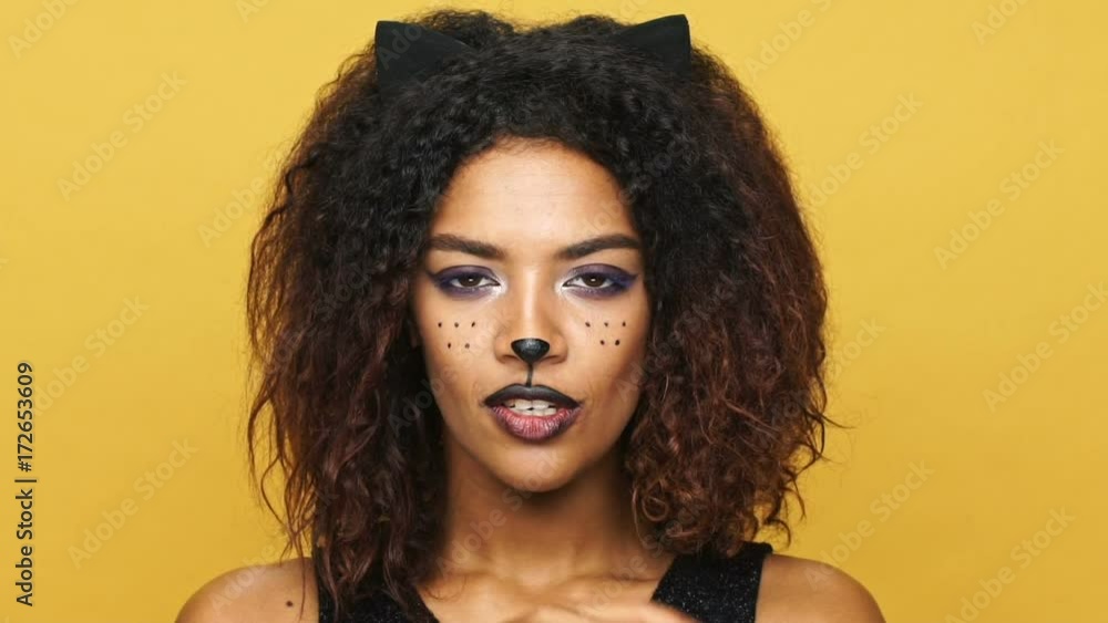 Serious calm african lady with cat ears showing silence gesture isolated over yellow Serious calm african lady with cat ears showing silence gesture isolated over yellow