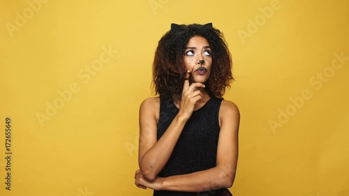 Thoughtful tricky lady with cat make-up thinking and having idea isolated over yellow background photo