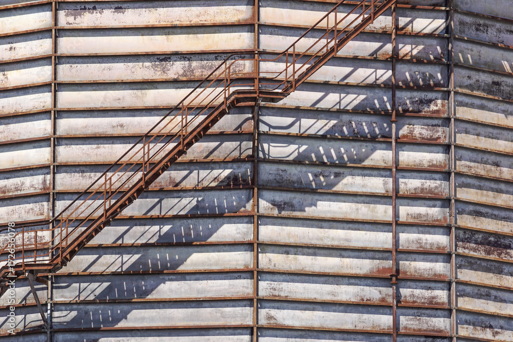 Concrete cylindrical industrial silo with metal stairs with safety railing and large bore pipes.