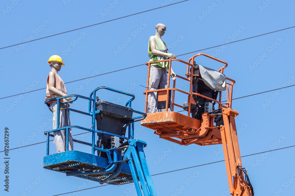 Hydraulic mobile construction platform elevated towards a blue sky with false construction workers . dummy man