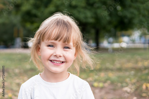Portrait of a small laughing blond girl in nature with blurred background