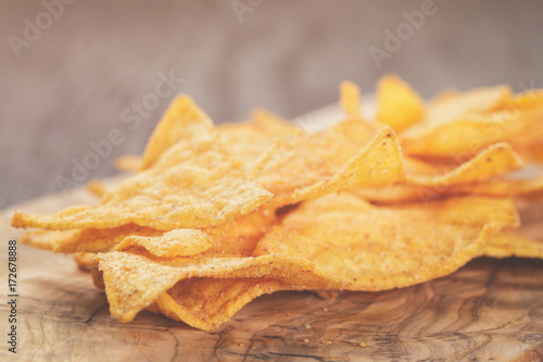 heap of tortilla chips on olive board on wooden table