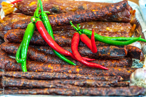 A lot of smoked domestic sausages and pods of chili peppers photo