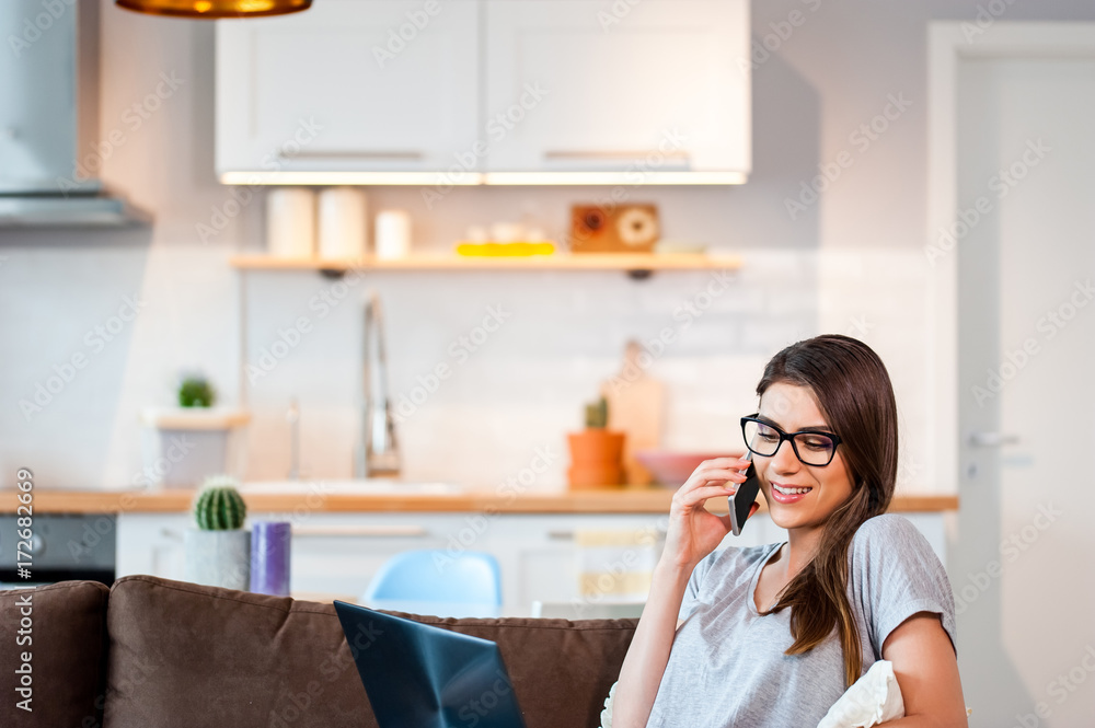 Casual young woman in a modern decorated home interior sitting comfortable on the couch using phone with laptop. Casual young woman in a modern decorated home interior sitting comfortable on the couch using phone with laptop.