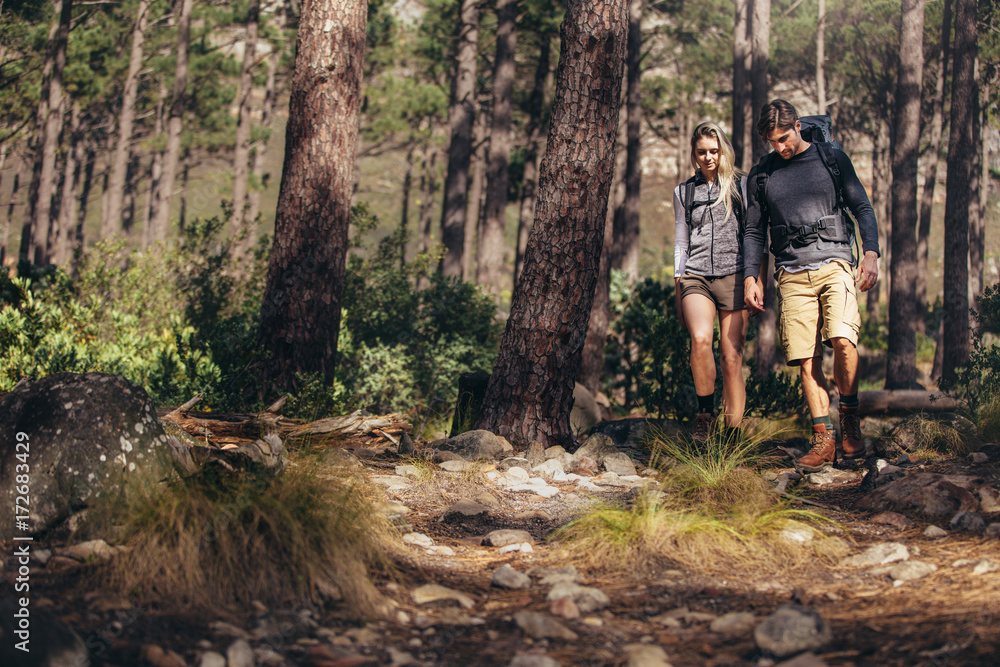 Hiking couple walking on rocks in forest wearing backpacks Hiking couple walking on rocks in forest wearing backpacks
