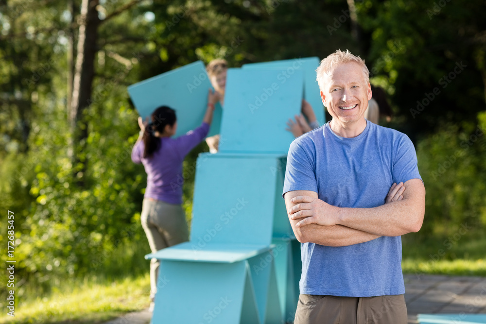 Naklejka premium Mature Man Standing Arms Crossed While Friends Making Planks Pyr