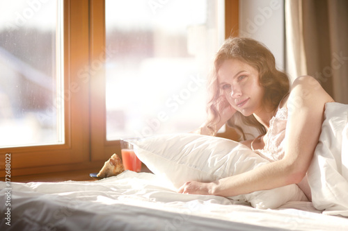Woman lying in bed at early morning near window.