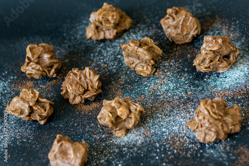 Close up of home-made chocolate candies. Harmony of crispy cornflakes and sweet chocolate, sprinkled with sugar and cocoa. Shallow depth of focus.