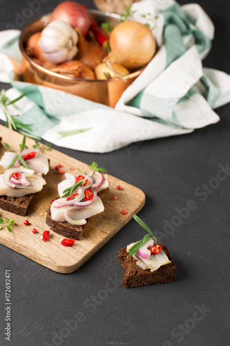 Sandwich with herring, black bread, black background, hot pepper, pickled onion, vertical, selective focus