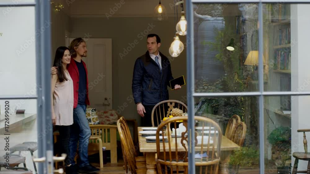 Couple with real estate agent, looking at home to buy or rent, view from outside looking in through open door. Couple with real estate agent, looking at home to buy or rent, view from outside looking in through open door.