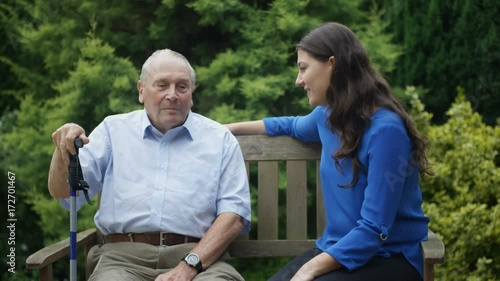 Young female relative visiting senior man in the garden at nursing home.