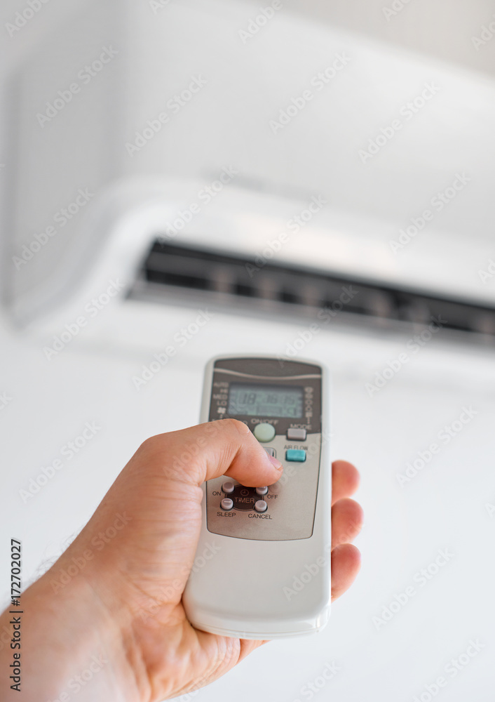Hand holding remote control aimed at the air conditioner. Hand holding remote control aimed at the air conditioner.