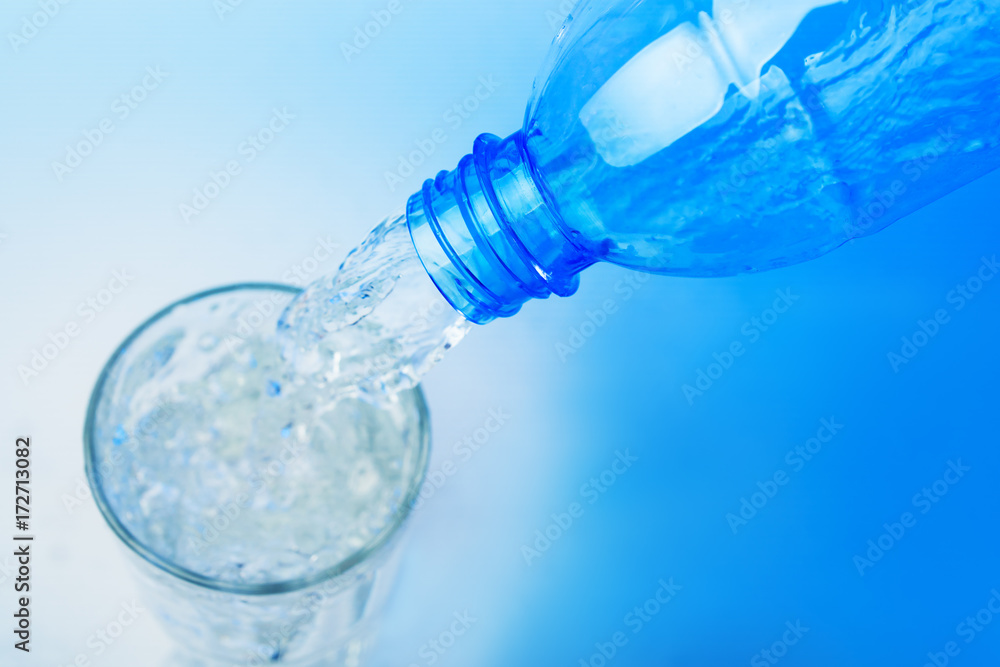 Close up shot : Pour water from plastic bottle in to the glass on blue backgroud Close up shot : Pour water from plastic bottle in to the glass on blue backgroud