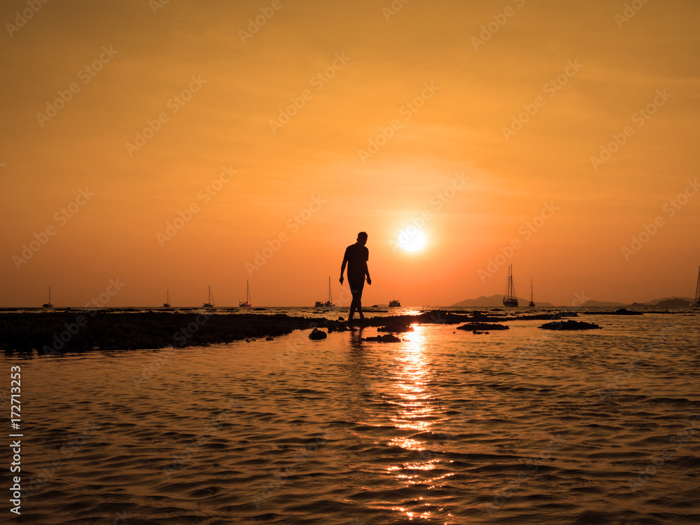 Silhouette of young man walk to the sun at sea beach with beautiful sky sunset background. To success find goal target and take action concept.