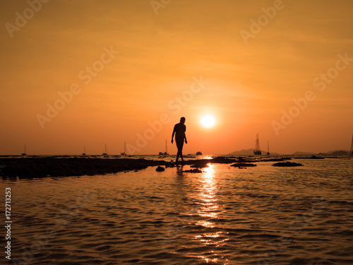 Silhouette of young man walk to the sun at sea beach with beautiful sky sunset background. To success find goal target and take action concept.