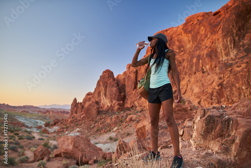 fit athletic african american woman drinking water in front of rock formation at valley of fire park