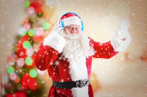 Santa Claus with headphones listening to Christmas music and snow effect on blurred background