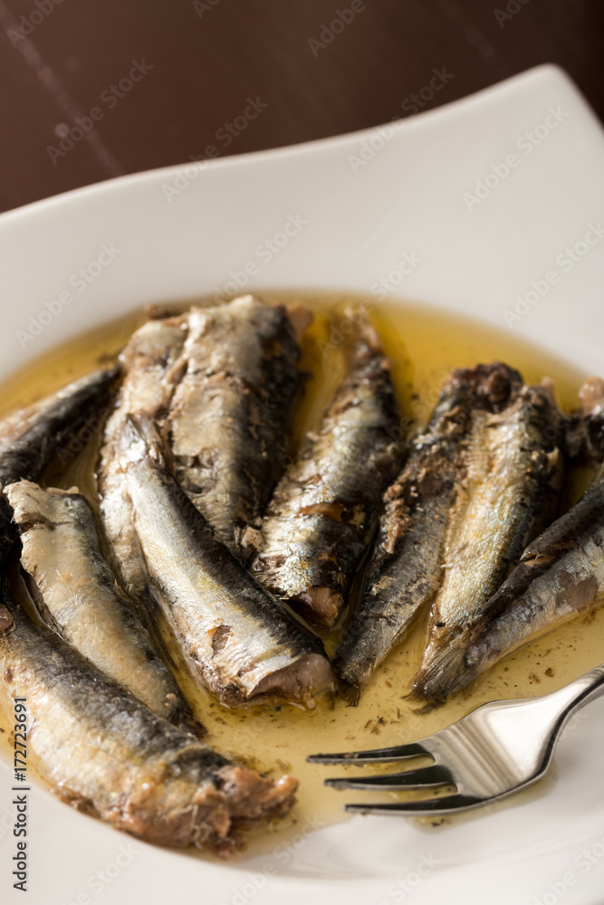 Closeup macro of marinated sardines in oil served on a white plate with a metal fork Closeup macro of marinated sardines in oil served on a white plate with a metal fork