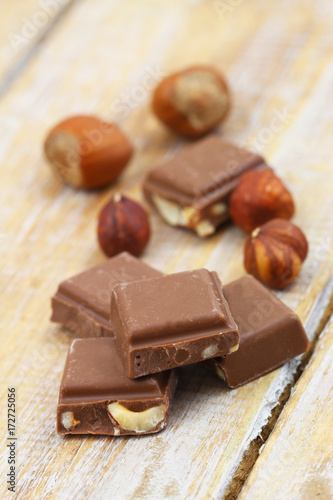 Pieces of crunchy chocolate with hazelnuts on rustic wooden surface
