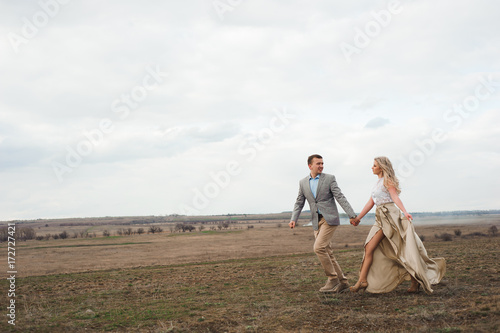 Handsome guy and blonde girl walking on the field, a man leads a woman holding the hand