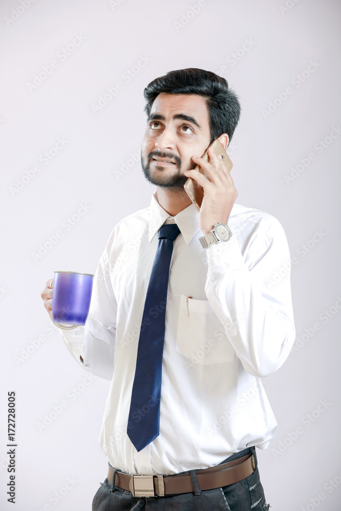 indian young man talking on cellphone and holding cup in hand