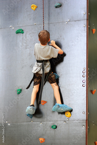 Five year old boy learning to climb the rock mountain wall in the summer park outside. Bouldering.