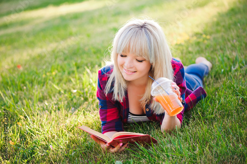 Girl drink juice and read a book in a park © nagaets