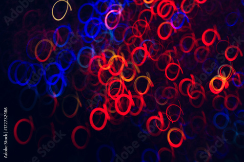 Abstract background of colorful circles in motion on black. Bokeh of defocused curls, blurred neon blue and red leds, glowing festive backdrop of night city lights