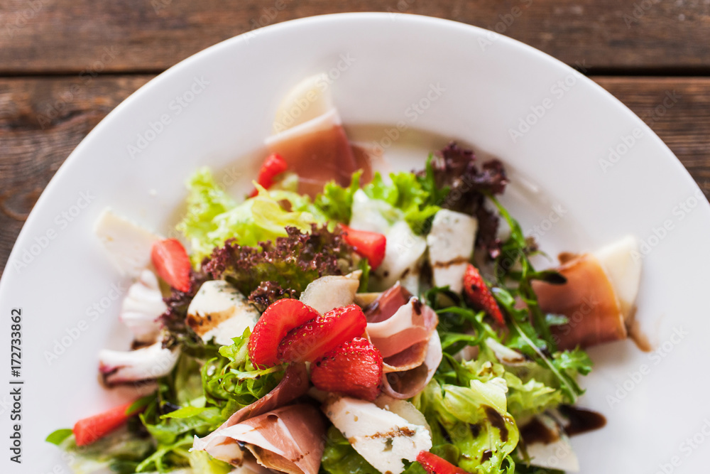 Fresh green salad with parma ham, blue cheese and strawberry serving in restaurant on wooden table. Gourmet cuisine close up top view picture