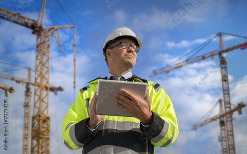 Construction engineer wearing safety vest with yellow crane on the background