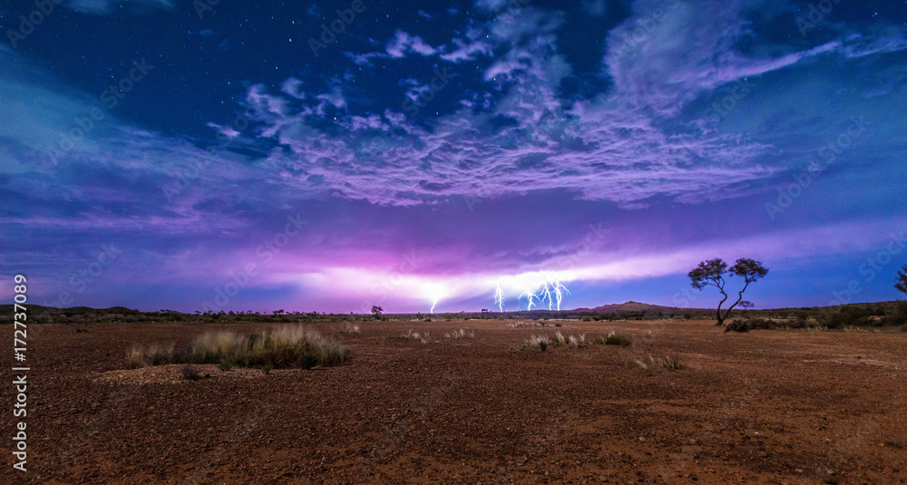 Five lightnings on a cloudy sky full of stars with the red dry soil of the outback desert under it. Thunderstorm lightning.