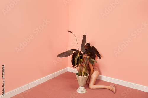 woman in a pink room hiding behind a plant