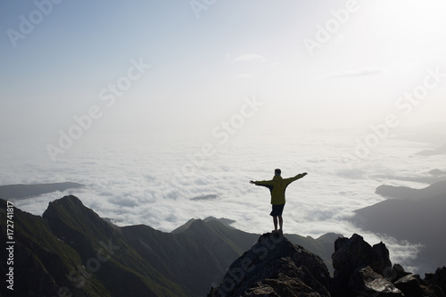 Young man silhouette with arms raised to fly over the clouds photo