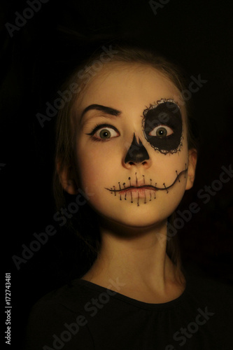 Halloween, holidays, masquerade concept - the portrait of young little beautiful girl with skull makeup on black background. Halloween, face-art, skull make up concept.
