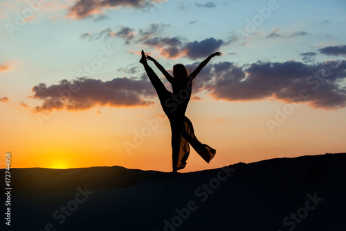Woman is dancing at sunset against the sky. The backlight of the sun only contours of the figures are visible.