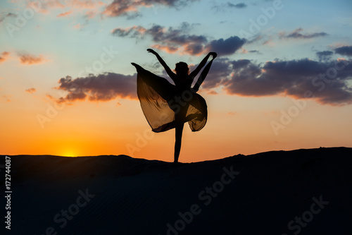 Fotografie Dancer at sunset against the sky, her dress fluttering
